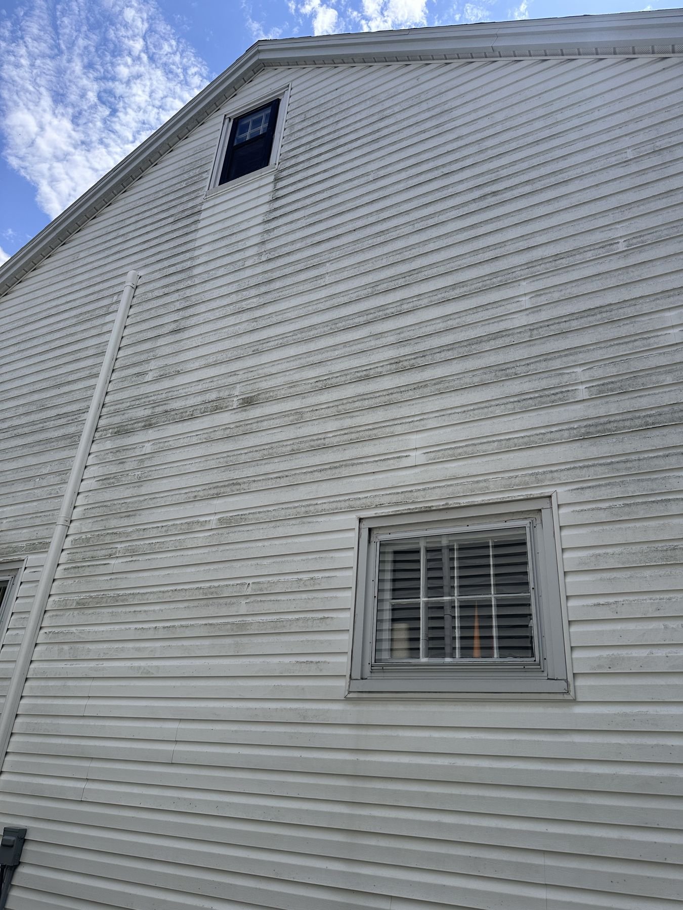 Gable-end vinyl siding with grey and black algae streaking around a window