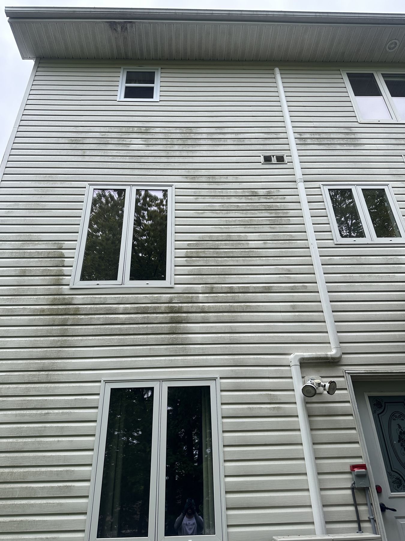 Vinyl siding on a two-storey Halifax home showing dark algae streaking down from the roofline