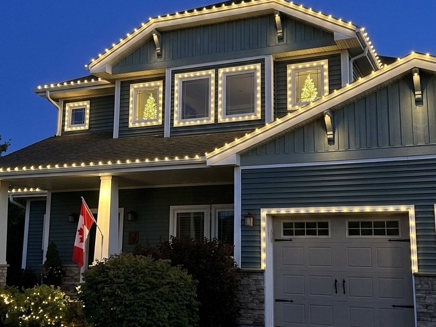 Halifax home with a warm-white roofline outline, lit window trees and glowing garden shrubs at dusk
